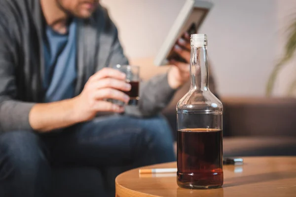 Bottle of whiskey near man holding photo frame on blurred foreground — Stock Photo