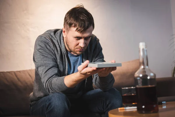 Depressed man sitting near table with alcohol drinks and holding photo frame — Stock Photo