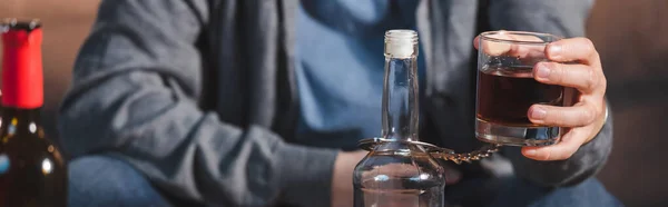 Vista recortada del hombre, esposado a la botella, sosteniendo vaso de whisky, pancarta - foto de stock