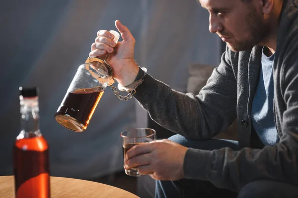 Homme accro, menotté à une bouteille de whisky, avant-plan flou — Photo de stock