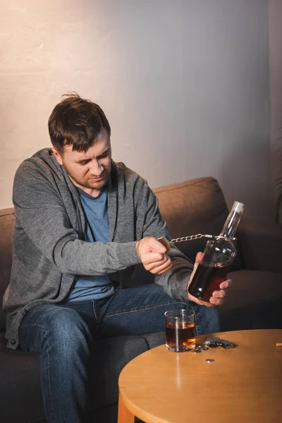 Alcohol-addicted man handcuffed to bottle of whiskey at home — Stock Photo