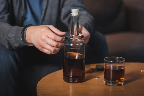 Vista recortada del hombre, esposado a la botella de whisky, sentado en casa solo - foto de stock