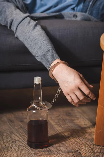 Vue recadrée de ivrogne, homme endormi, menotté à une bouteille de whisky — Photo de stock