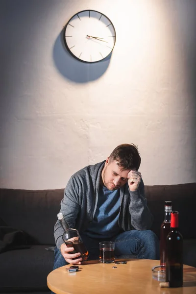 Hombre deprimido sosteniendo botella de whisky mientras está sentado en casa solo — Stock Photo