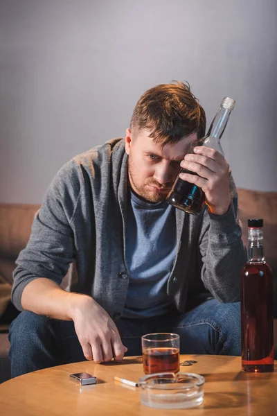 Drunk, alcohol-addicted man holding bottle of whiskey at home — Stock Photo