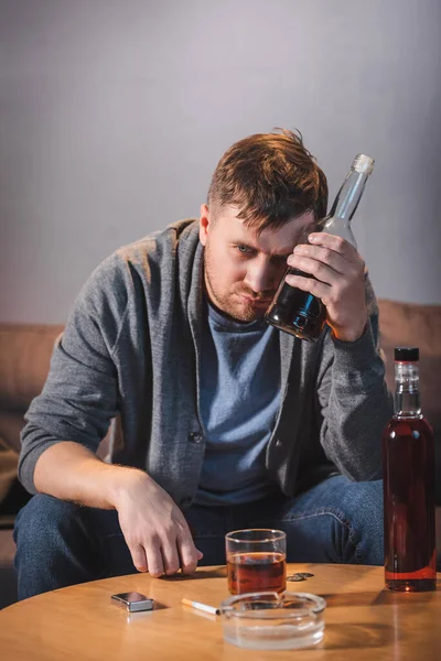 Drunk, alcohol-addicted man holding bottle of whiskey at home — Stock Photo