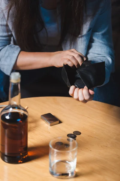 Ausgeschnittene Ansicht einer alkoholabhängigen Frau mit leerem Portemonnaie in der Nähe einer Flasche Whiskey im verschwommenen Vordergrund — Stockfoto