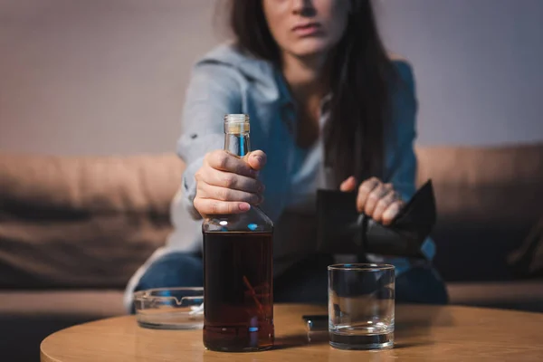 Abgeschnittene Ansicht einer süchtigen Frau, die eine Flasche Whiskey vom Tisch nimmt, verschwommener Hintergrund — Stockfoto