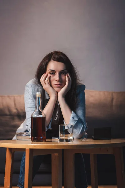 Depressed woman sitting near bottle of whiskey at home alone — Stock Photo