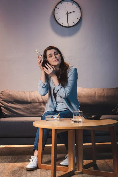 Bouleversée, femme ivre tenant une bouteille de vin près de la tête alors qu'elle était assise seule à la maison — Photo de stock