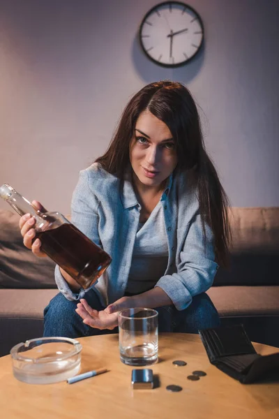 Alcohol-addicted woman looking at camera while holding bottle of whiskey — Stock Photo