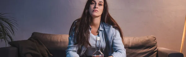 Frustrated woman looking at camera while sitting near bottle of alcohol, banner — Stock Photo