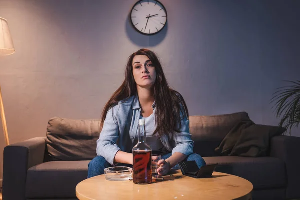 Alcohol-addicted woman sitting near bottle of whiskey and empty wallet at home — Stock Photo