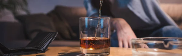 Cropped view of woman pouring whiskey into glass near empty wallet, banner — Stock Photo