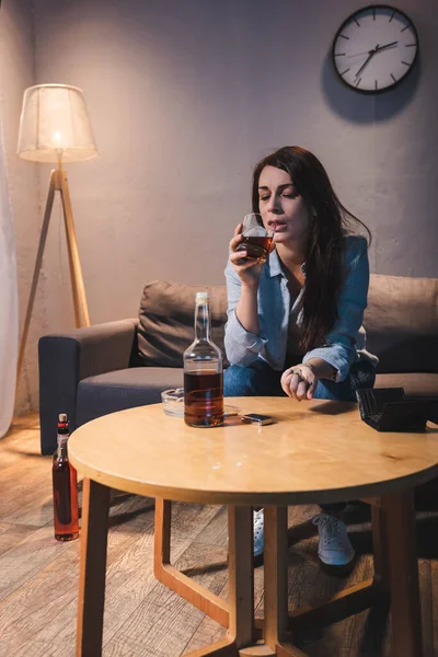 Einsame Frau trinkt Whiskey neben Flasche und leerem Portemonnaie auf Tisch — Stockfoto