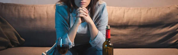 Vista ritagliata della donna alcolizzata seduta vicino alla bottiglia e al bicchiere di vino rosso, striscione — Foto stock