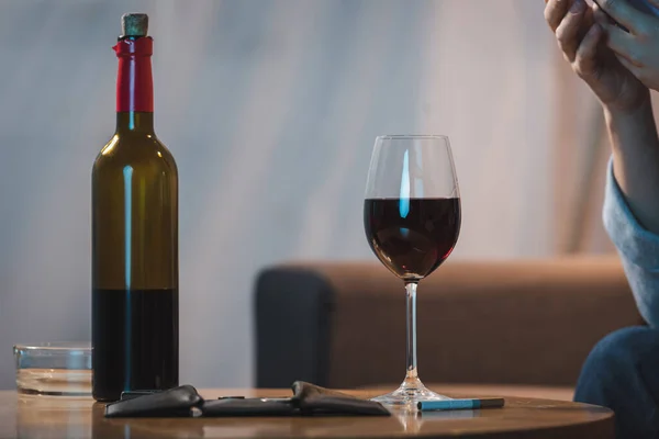 Vista recortada de la mujer adicta al alcohol cerca de botella y vaso de vino tinto - foto de stock