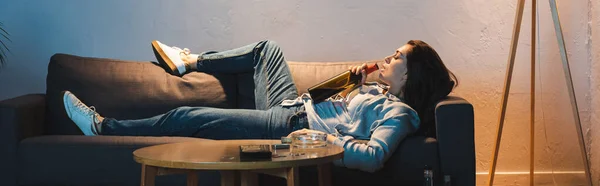 Алкогольна жінка п'є вино з пляшки, лежачи на дивані, банер — стокове фото
