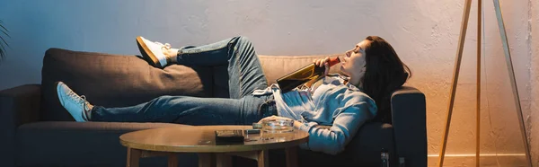 Alcoholic woman drinking wine from bottle while lying on sofa, banner — Stock Photo