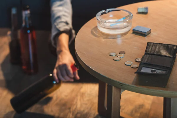 Vista parcial de la mano femenina con botella de alcohol cerca de monedas y billetera vacía en la mesa, fondo borroso - foto de stock