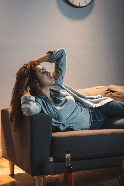 Depressive, alkoholabhängige Frau liegt auf Sofa neben Flaschen auf dem Boden — Stockfoto