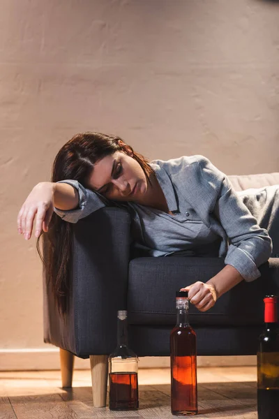 Frustrated, drunk woman lying on sofa near bottles on floor — Stock Photo