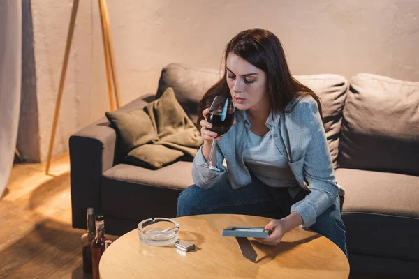 Alcoholic woman drinking red wine while sitting at home alone and holding photo frame — Stock Photo