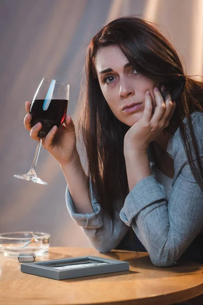 Frustrated woman looking away while sitting near photo frame with glass of red wine — Stock Photo