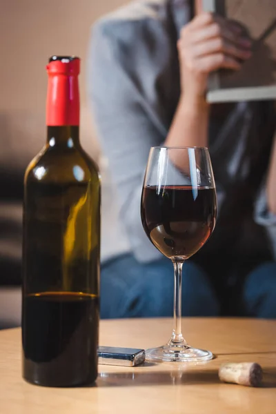 Glass and bottle of red wine near alcohol-addicted woman on blurred background — Stock Photo