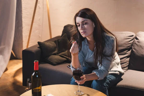 Алкогольна залежна жінка тримає обручку, сидячи за келихом червоного вина — стокове фото