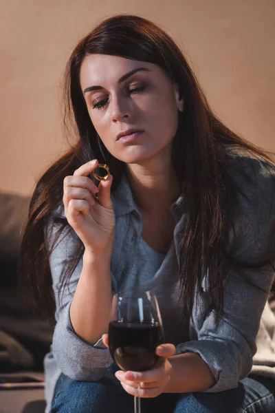 Drunk woman holding wedding ring and glass of red wine while sitting at home alone — Stock Photo