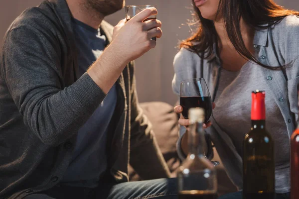 Vista recortada de la pareja bebiendo whisky y vino cerca de botellas en primer plano borroso - foto de stock