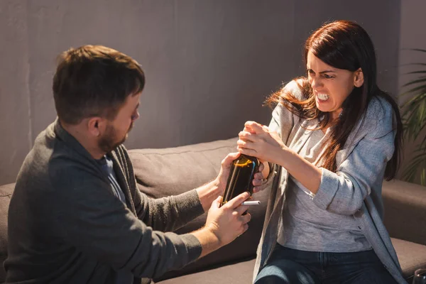 Homme emportant bouteille de vin d'agressif, alcoolique femme accro à la maison — Photo de stock