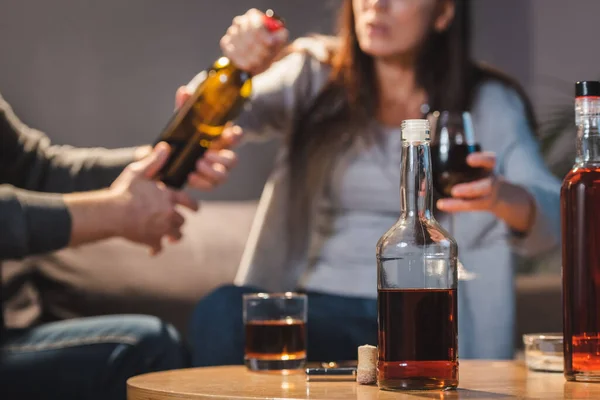 Vista recortada del hombre quitando botella de vino de la esposa cerca de la mesa con bebidas alcohólicas, fondo borroso - foto de stock