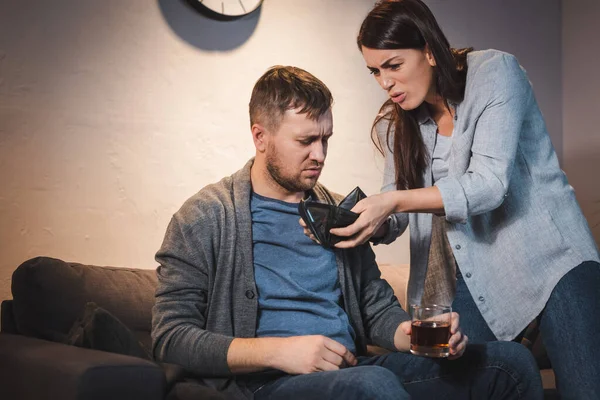 Irritated woman showing empty wallet to drunk man holding glass of whiskey — Stock Photo