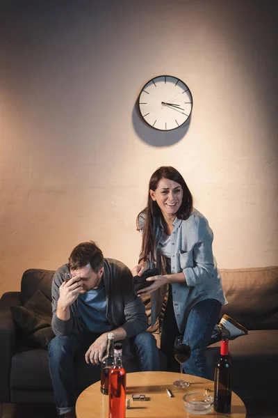 Weinende Frau mit leerer Brieftasche neben betrunkenem Mann und Tisch mit Flaschen — Stockfoto