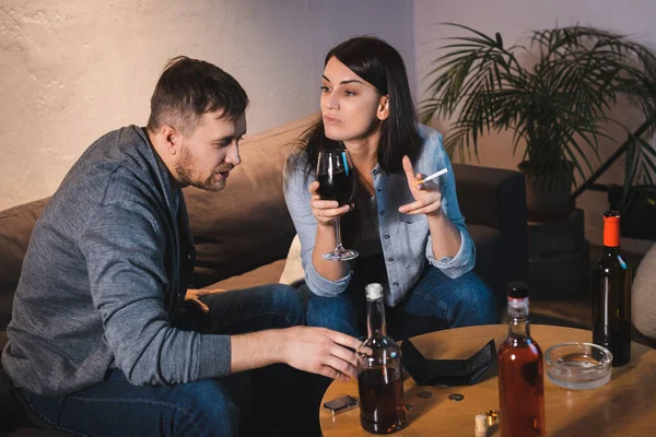 Mari ivre et femme assis à table avec des bouteilles et portefeuille vide — Photo de stock