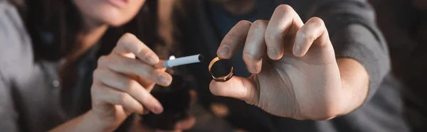 Cropped view of alcohol-addicted husband and wife holding wedding ring and cigarette, blurred background, banner — Stock Photo