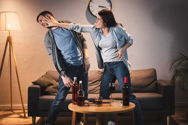 Femme ivre se battant avec mari près de la table avec des boissons alcoolisées à la maison — Photo de stock
