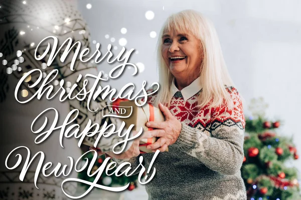 Cheerful senior woman presenting gift to husband near merry christmas and happy new year lettering — Stock Photo