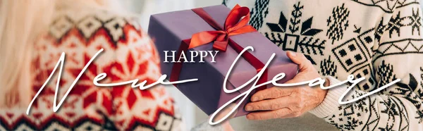 Vista ritagliata di uomo anziano che presenta regalo di Natale alla moglie vicino felice anno nuovo lettering, banner — Foto stock