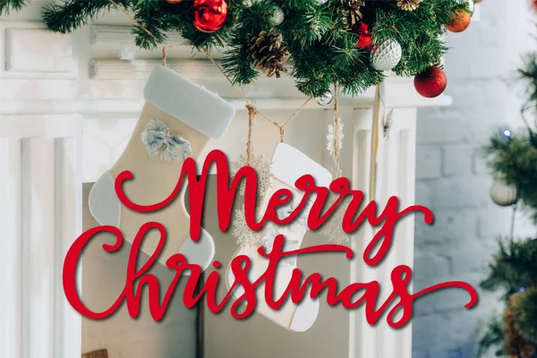 Rama de pino decorado con medias cerca de la chimenea y Feliz Navidad letras en casa - foto de stock