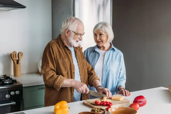 Sonriente anciana esposa mirando marido cocina cena en cocina — Stock Photo