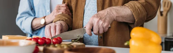 Vista recortada de anciana cerca de hombre cortando queso en la mesa con verduras en primer plano borroso, pancarta — Stock Photo