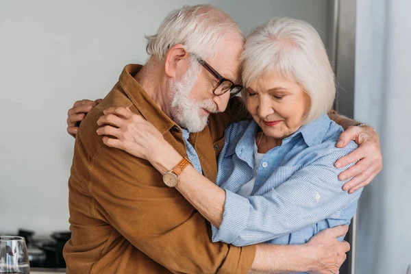 Glückliches Seniorenpaar mit geschlossenen Augen, das sich drinnen umarmt — Stockfoto