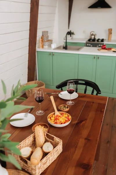 Mesa servida con cena vegetariana y copas de vino en cocina con planta borrosa en primer plano - foto de stock