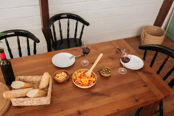 Vista ad alto angolo del tavolo servito con cena vegetariana, baguette in cesto e vino in cucina — Foto stock