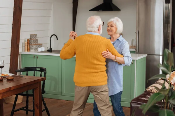 Vista trasera de anciano marido bailando con feliz esposa en cocina - foto de stock