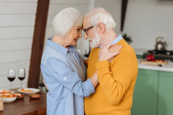 Sonriente pareja de ancianos mirándose mientras bailan en la cocina sobre un fondo borroso — Stock Photo