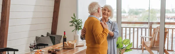 Sorridente coppia anziana che balla vicino al tavolo con cena vegetariana in cucina, striscione — Foto stock